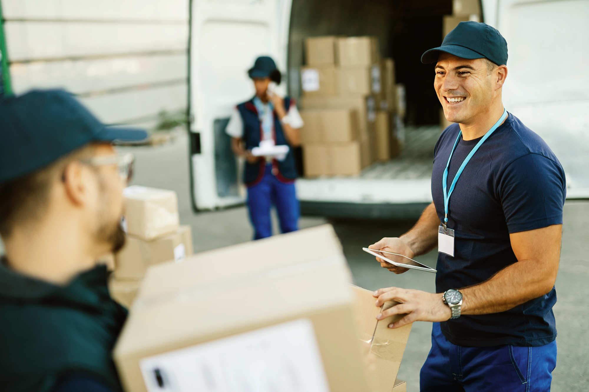 Happy manual worker using touchpad while communicating with his coworker and organizing package delivery.